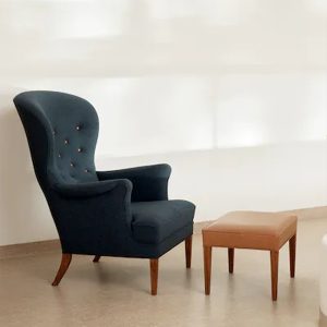 Billede af Heritage Chair er designet af Frits Henningsen (1889-1965), og det er en af hans kendteste. Stolen er med klassisk fuldpolstring, og med stel i massivt træ. En matchende fodskammel fuldender komforten.